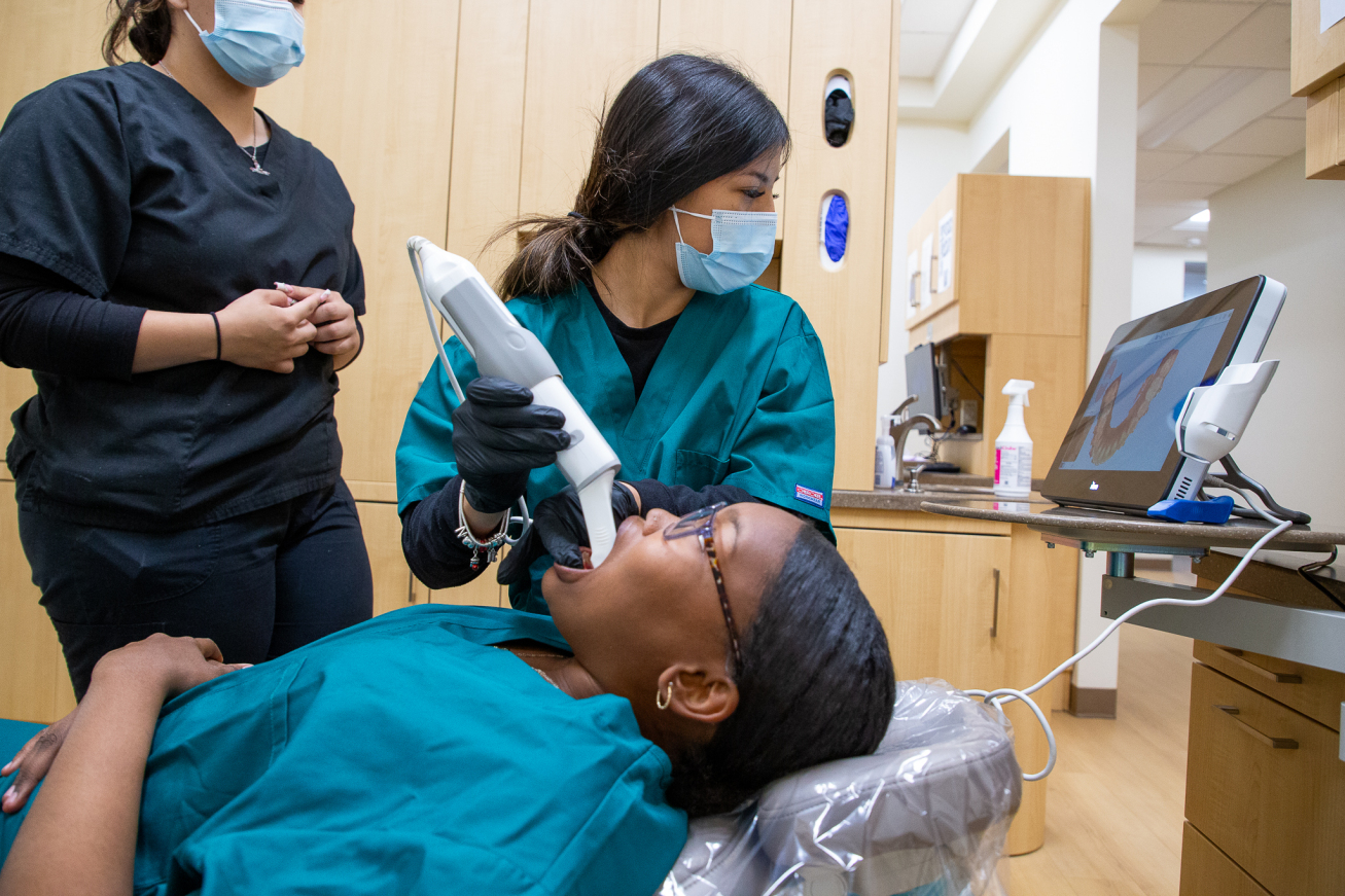 A dental tech works in a student's mouth to show fellow students how the scanner tool works