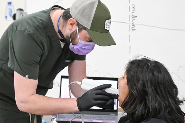 A man in scrubs and a mask demonstrates a dental scanning technique on a student's mouth