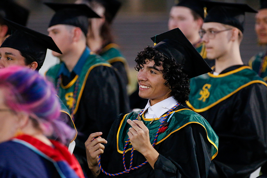 A teen boy smiles in his cap and gown during the ceremony