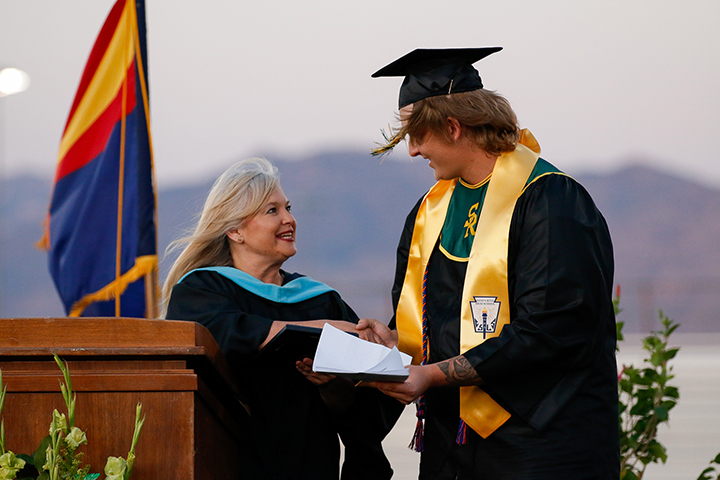 A graduate in his cap and gown shakes a woman's hand on stage