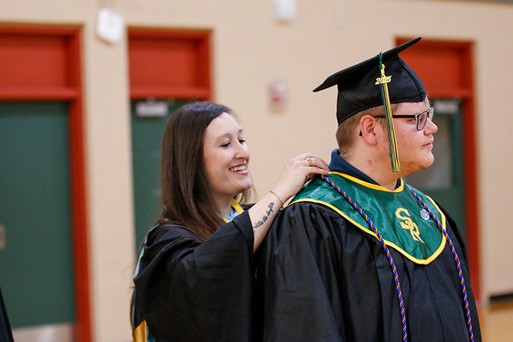 A woman adjusts a graduate's sash