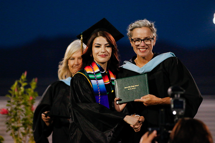 A graduate proudly holds her diploma with her principal