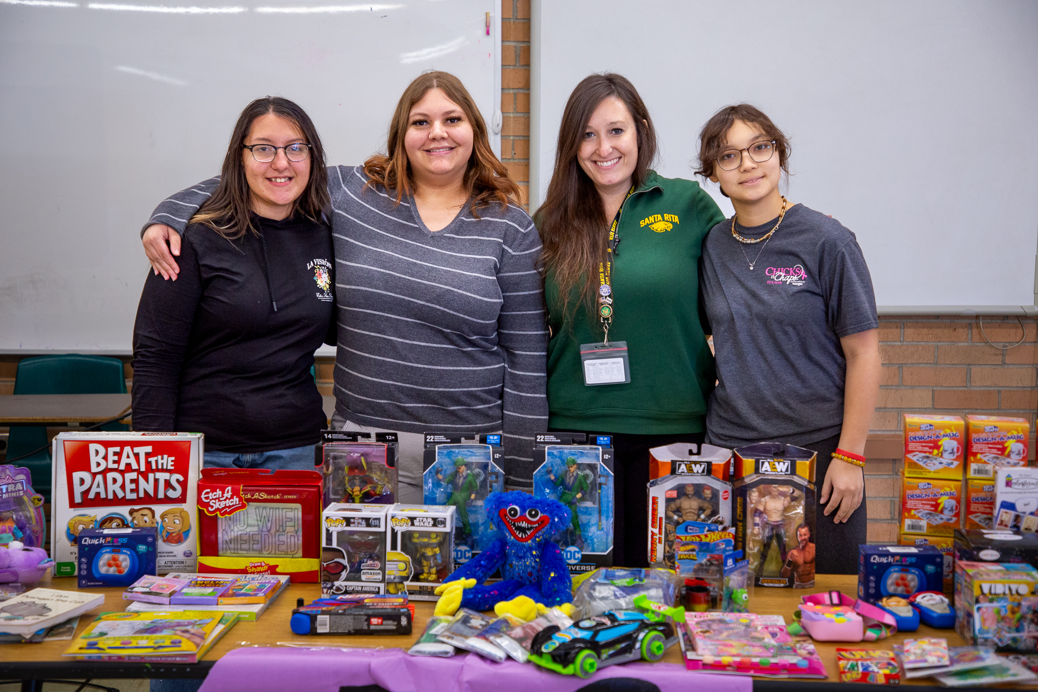 Four young women smile behind a table filled with toys