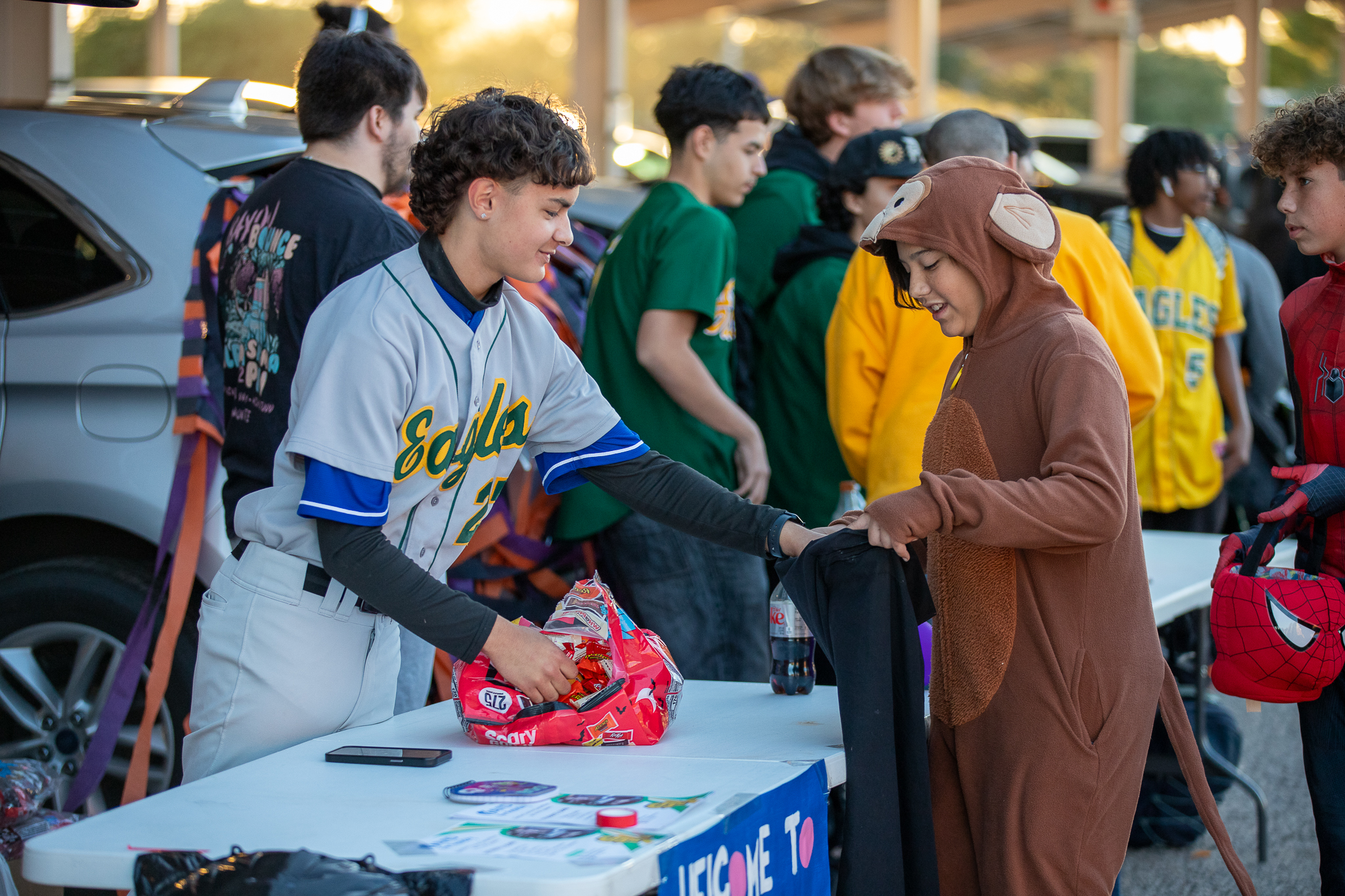 A student wearing an Eagles baseball jersey hands out candy to a kid in a monkey jumpsuit