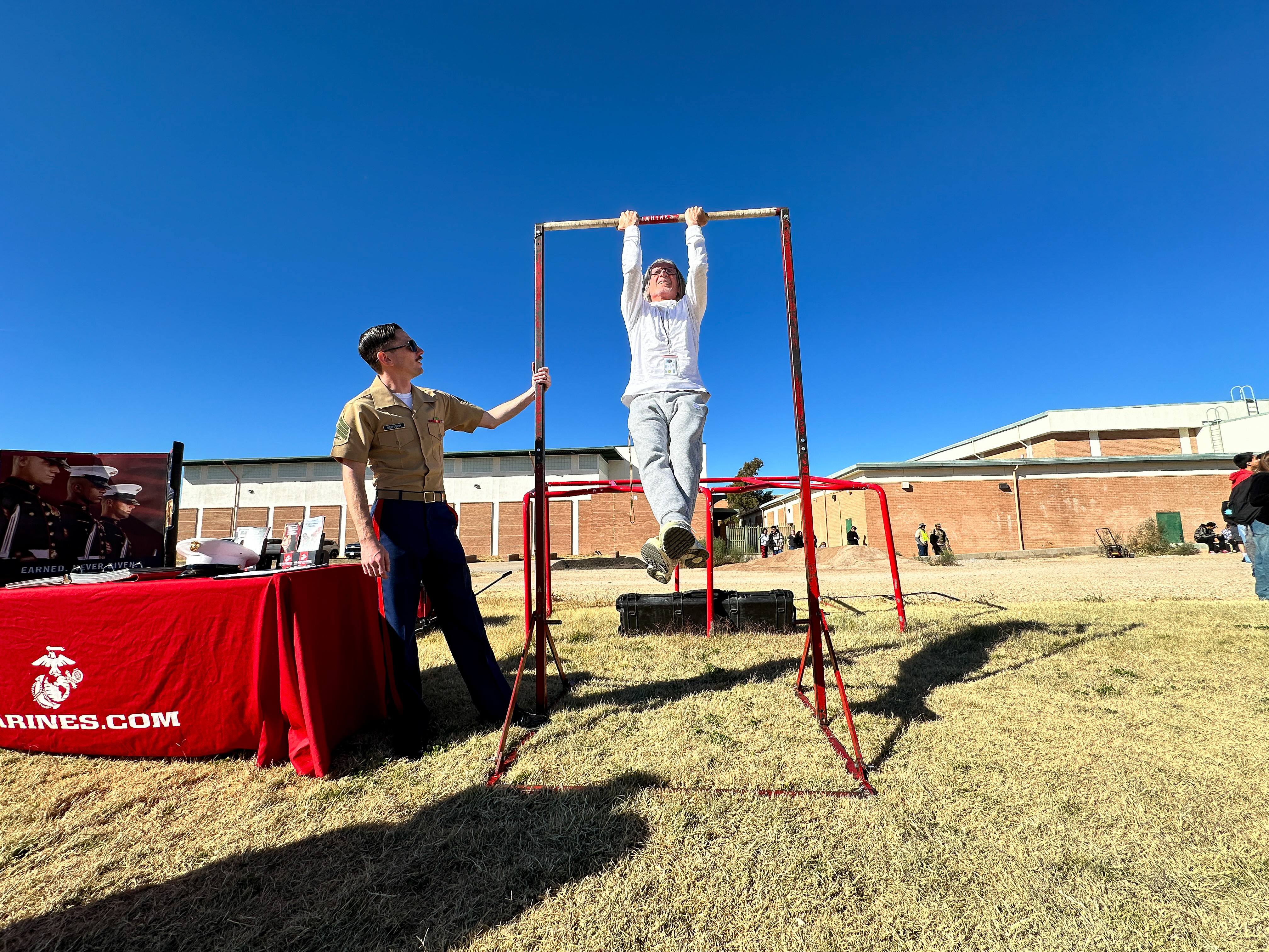 A woman attempts a pull-up while a Marine looks on