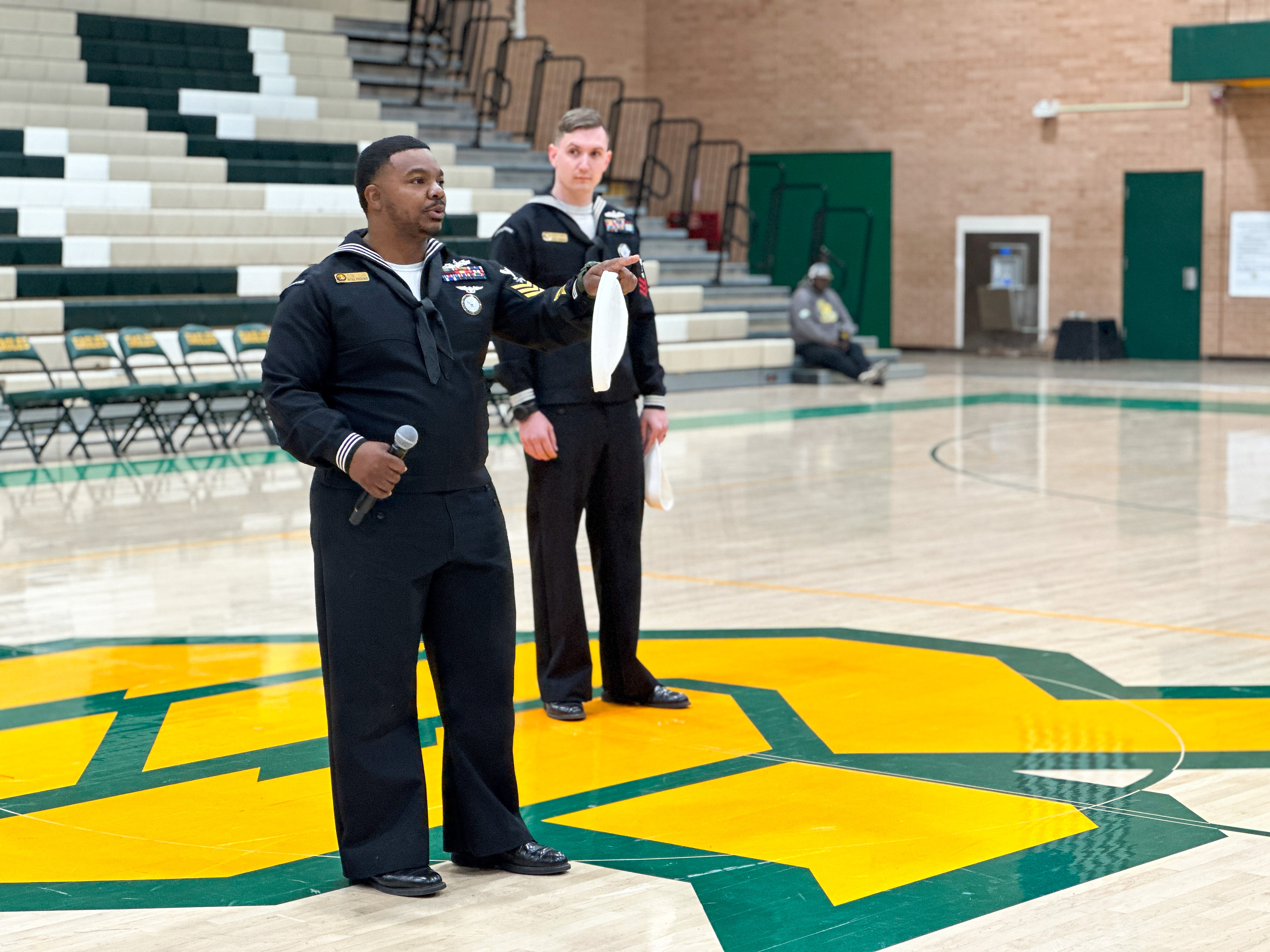 Two men in Navy uniforms talk to students in the gym