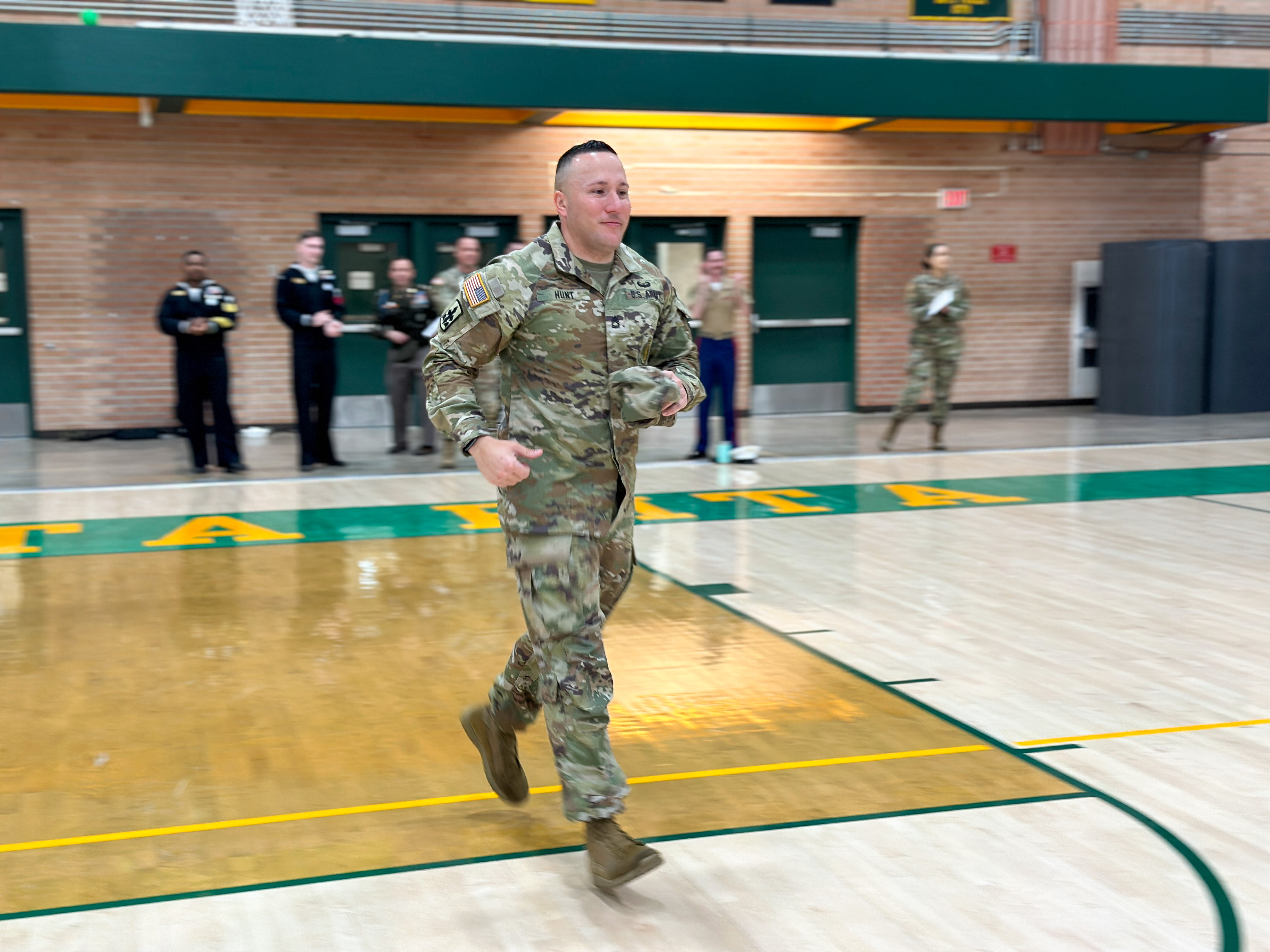 A servicemember in fatigues runs across the gym floor