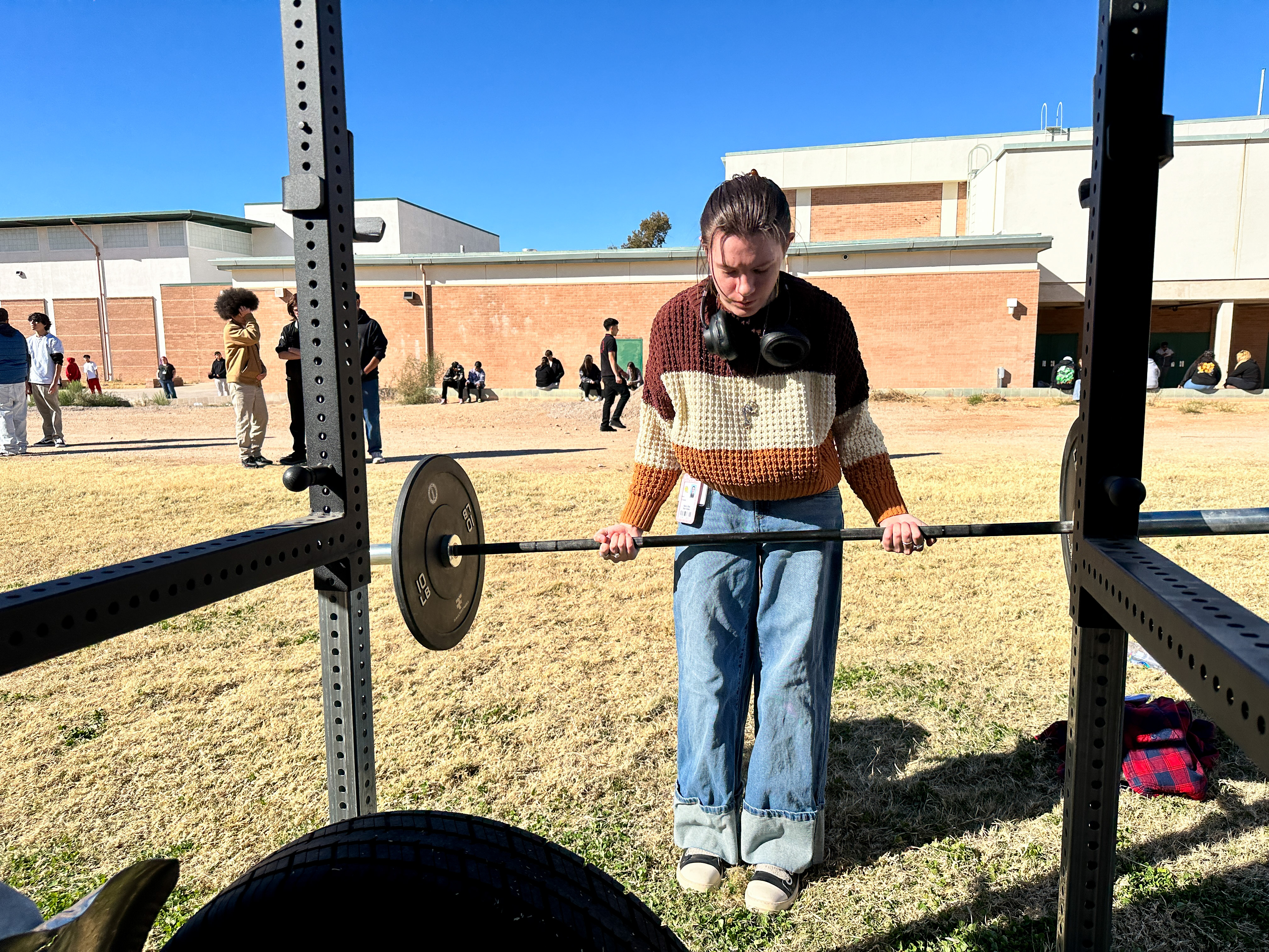 A girl lifts a barbell outside on the field