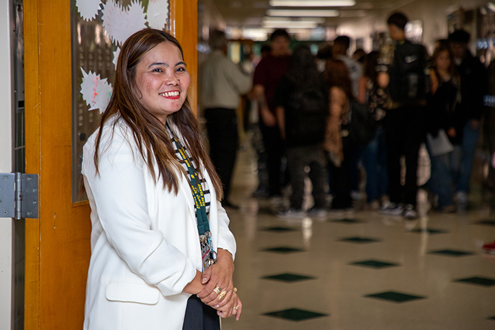 A woman smiles in front of a door to a hallway filled with students