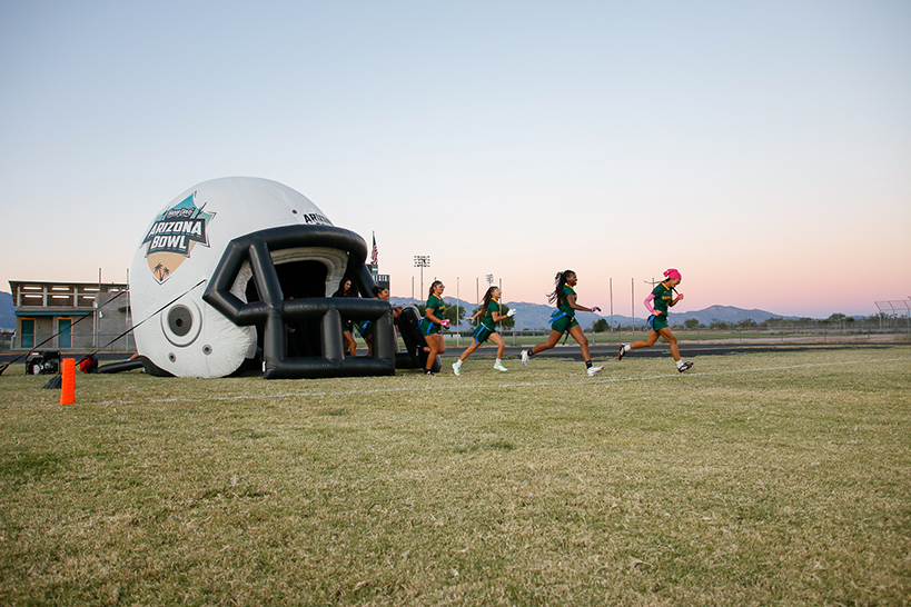 The girls flag football team runs out onto the field from the inflatable helmet