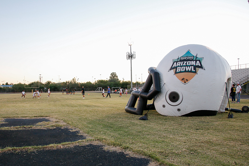 The girls flag football team plays their game on the field, with the inflatable Arizona Bowl helmet sitting on one end of the field