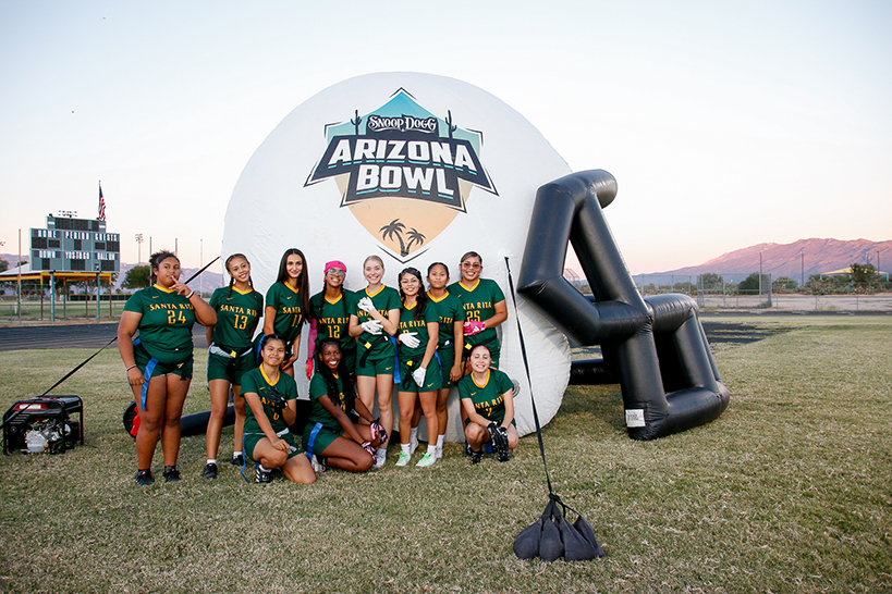 The girls flag football team poses for a group photo outside the inflatable Arizona Bowl helmet