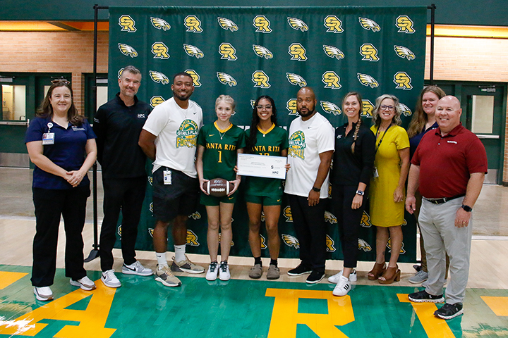A group of adults and two teen girls, center, hold up a donation check