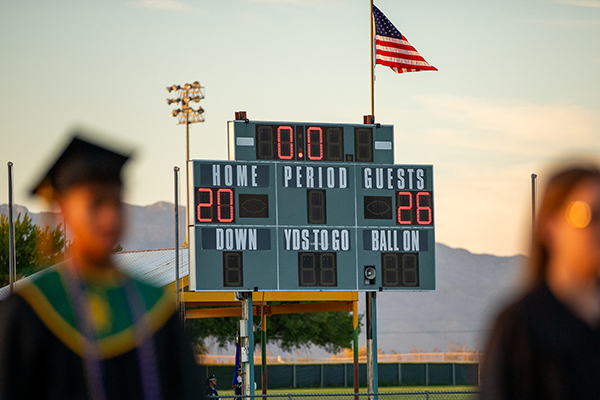 Graduates walk in front of the scoreboard during the ceremony