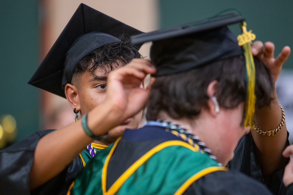 A teen boy adjusts his friend's graduation cap